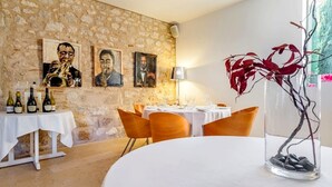 Un comedor con paredes de piedra, obras de arte enmarcadas, una mesa con botellas de vino y un jarrón con ramas.