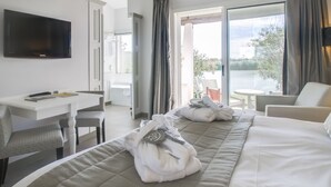 A hotel room with a bed, a desk, a chair, a TV, and a view of the outdoors. - L'estelle en Camargue (Saintes-Maries-de-la-Mer)