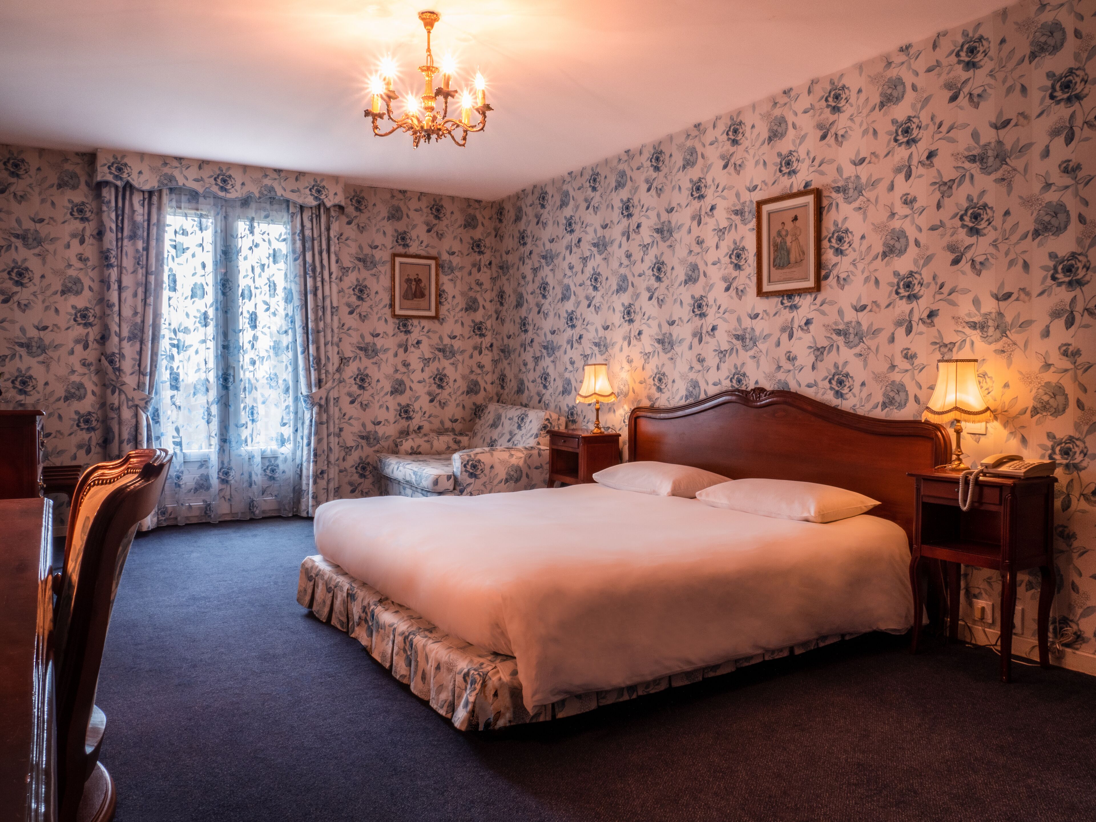 Ein Schlafzimmer mit einem großen Bett, zwei Nachttischlampen, einem Holznachttisch, einem Sessel und einer Deckenleuchte.