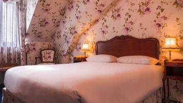 A bedroom with a large bed, floral wallpaper, two bedside lamps, a wooden nightstand, and a chair.
