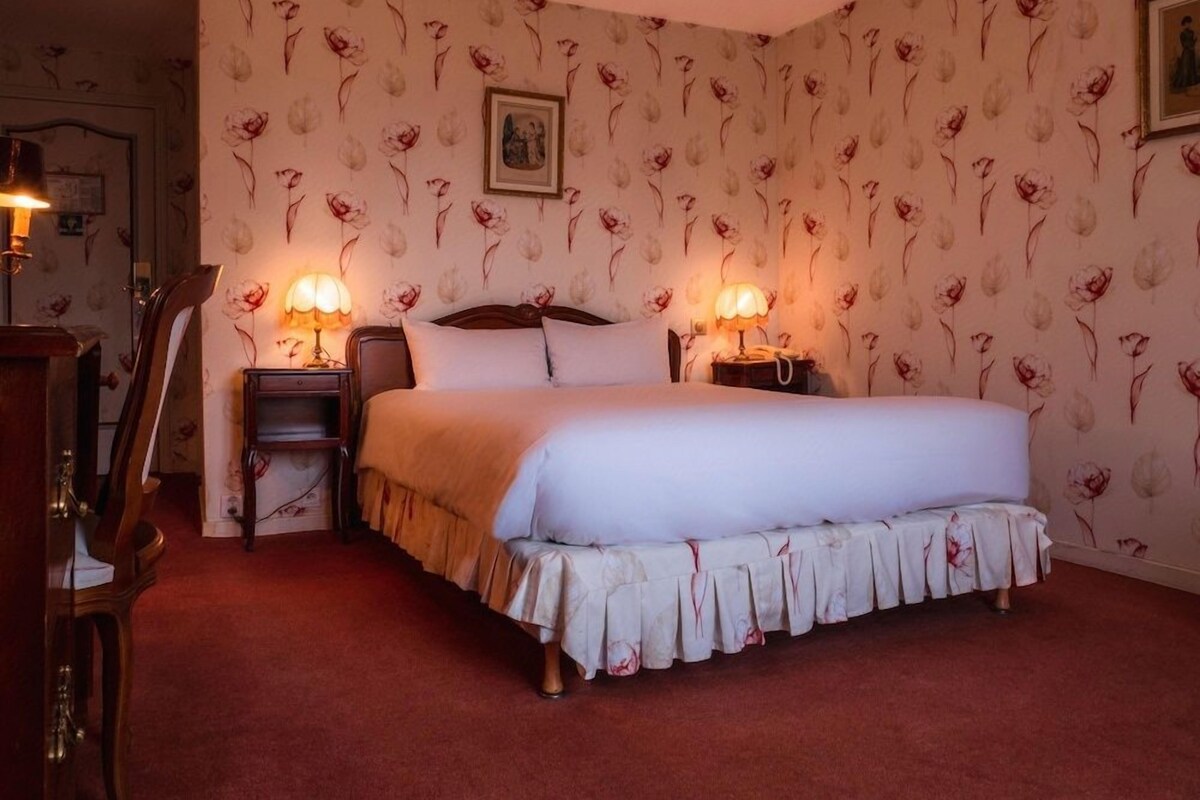 A bedroom with a large bed, two bedside tables with lamps, a wooden headboard, and floral wallpaper.