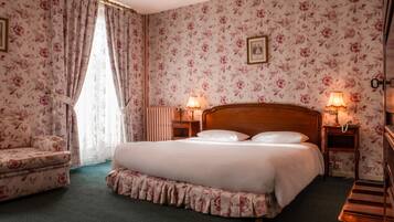 Un dormitorio con una cama grande, papel tapiz con motivos florales, una silla y lámparas de noche.