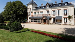 A large, historic building with a prominent tower, a covered porch, and a well-maintained garden with red flowers. - Château Des Bondons EI (La Ferte-sous-Jouarre)