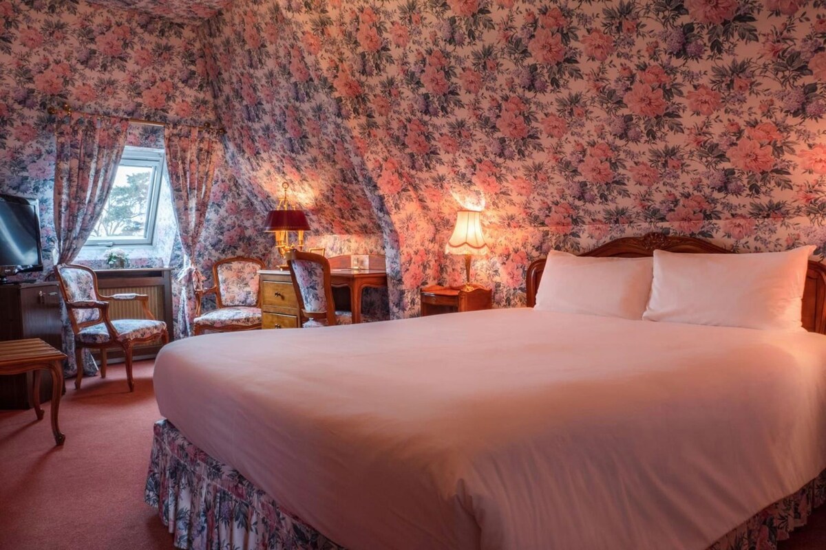 A bedroom with a large bed, a desk, a chair, and a lamp.