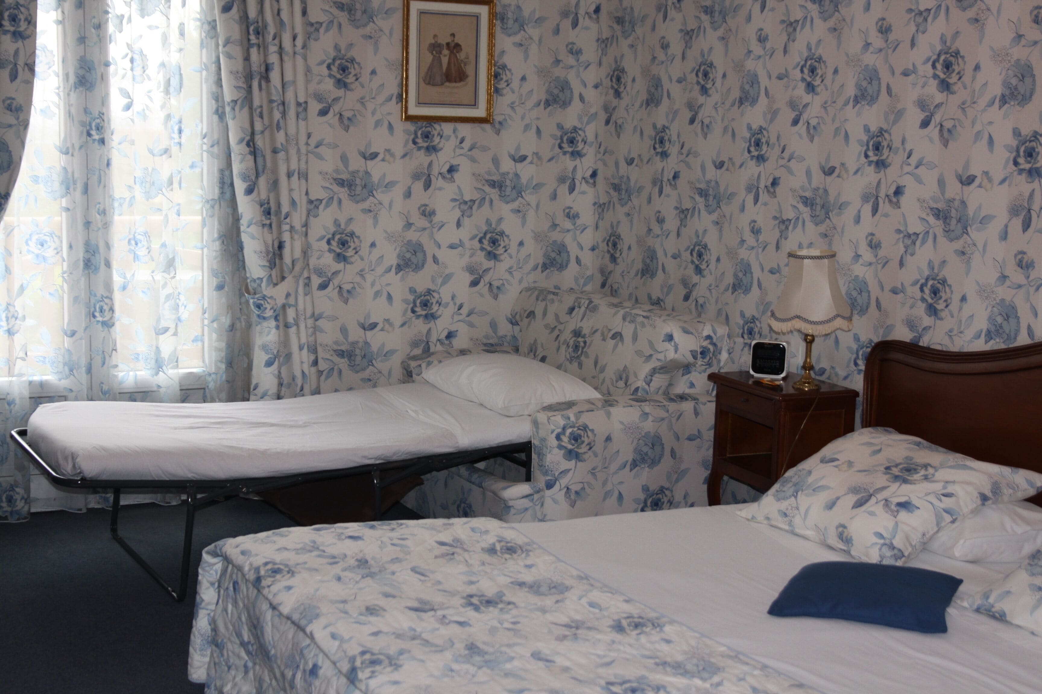 Une chambre avec deux lits, une table de chevet avec une lampe et un papier peint à motifs floraux.