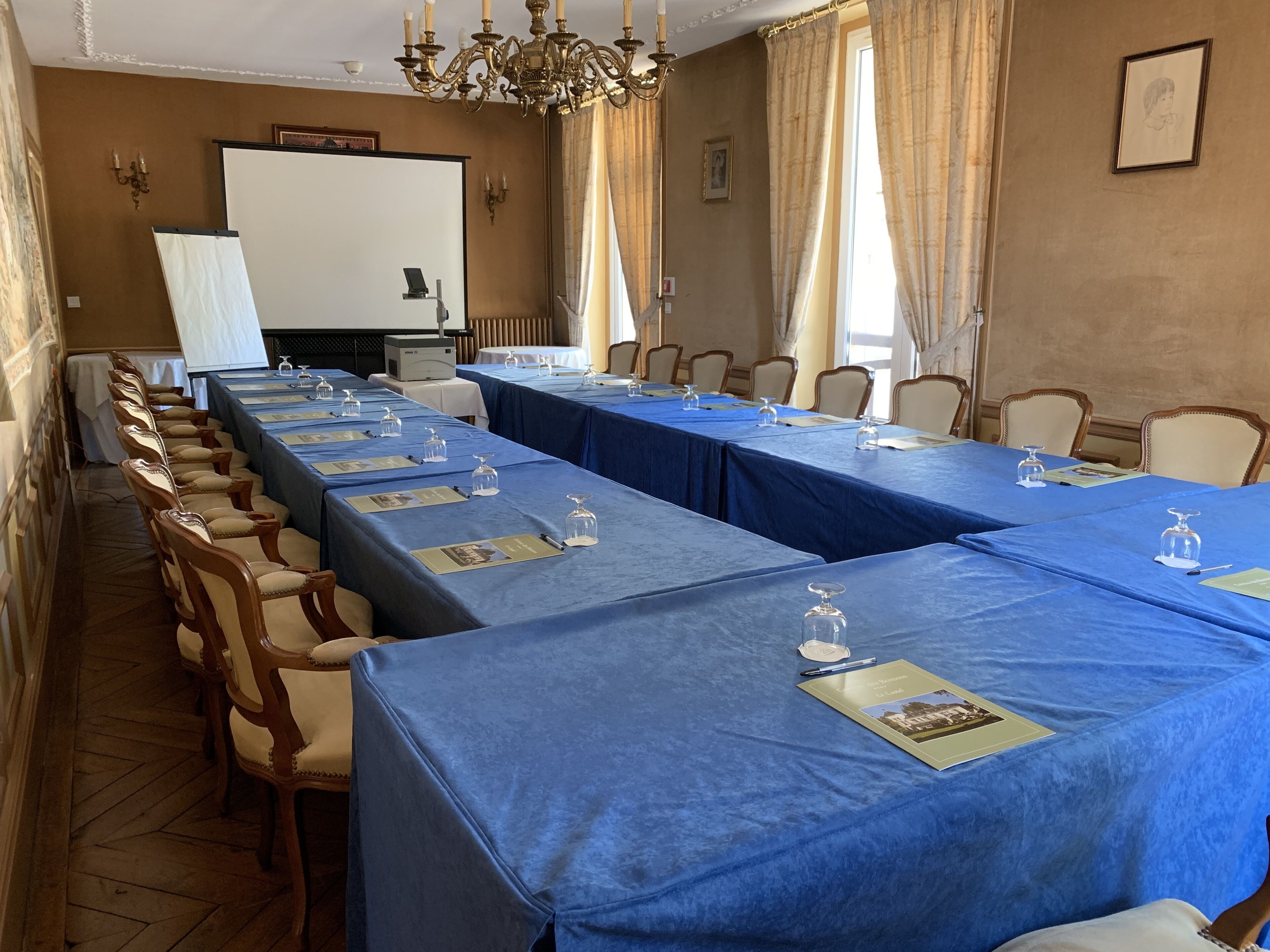 A conference room with long tables, chairs, a projector, and a chandelier.