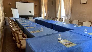 A conference room with long tables, chairs, a projector, and a chandelier.