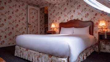 Une chambre à coucher avec un grand lit, un papier peint à motifs floraux, une tête de lit en bois, deux lampes de chevet et une table de chevet avec un téléphone.