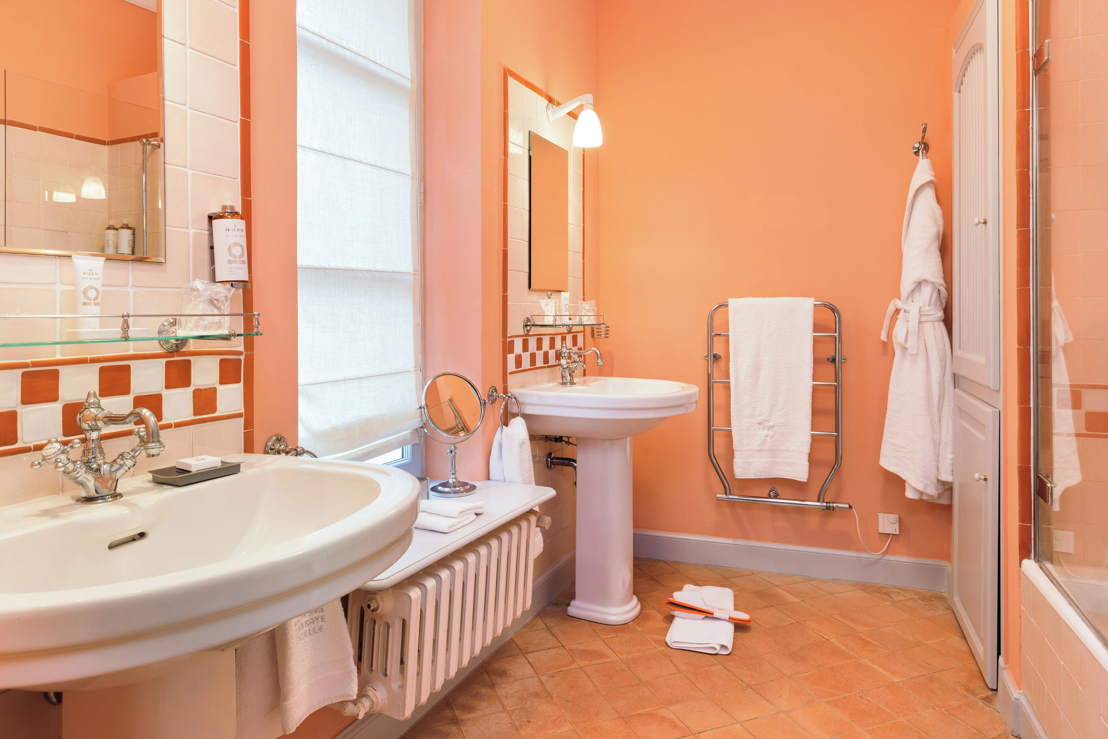 A bathroom with two sinks, a pedestal sink, a mirror, a towel rack, and a shower area.