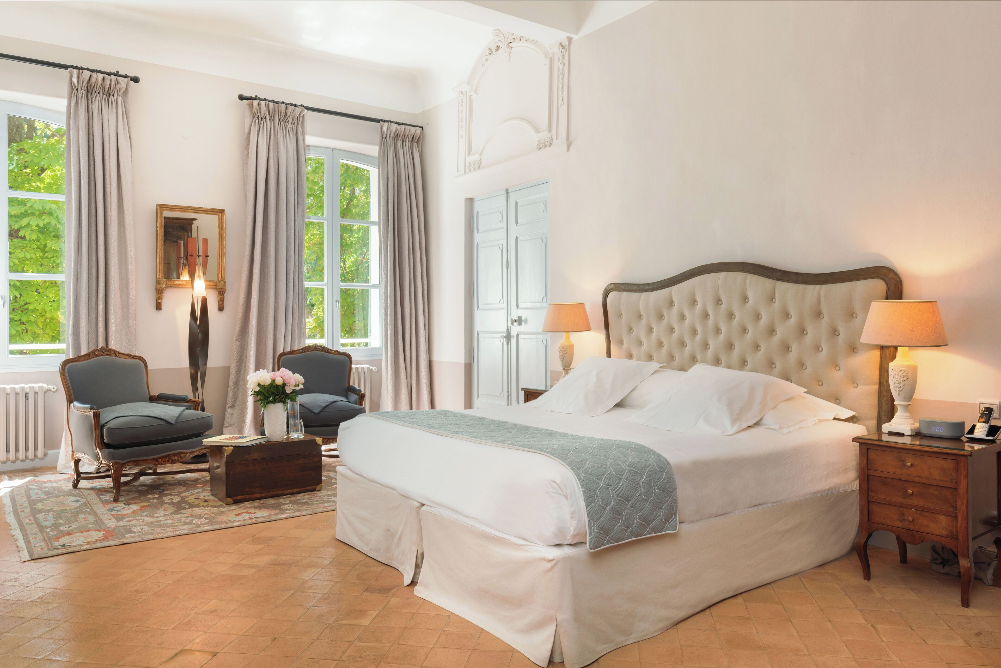 Une chambre spacieuse avec un grand lit, deux fauteuils, une petite table et une table de chevet avec des lampes.