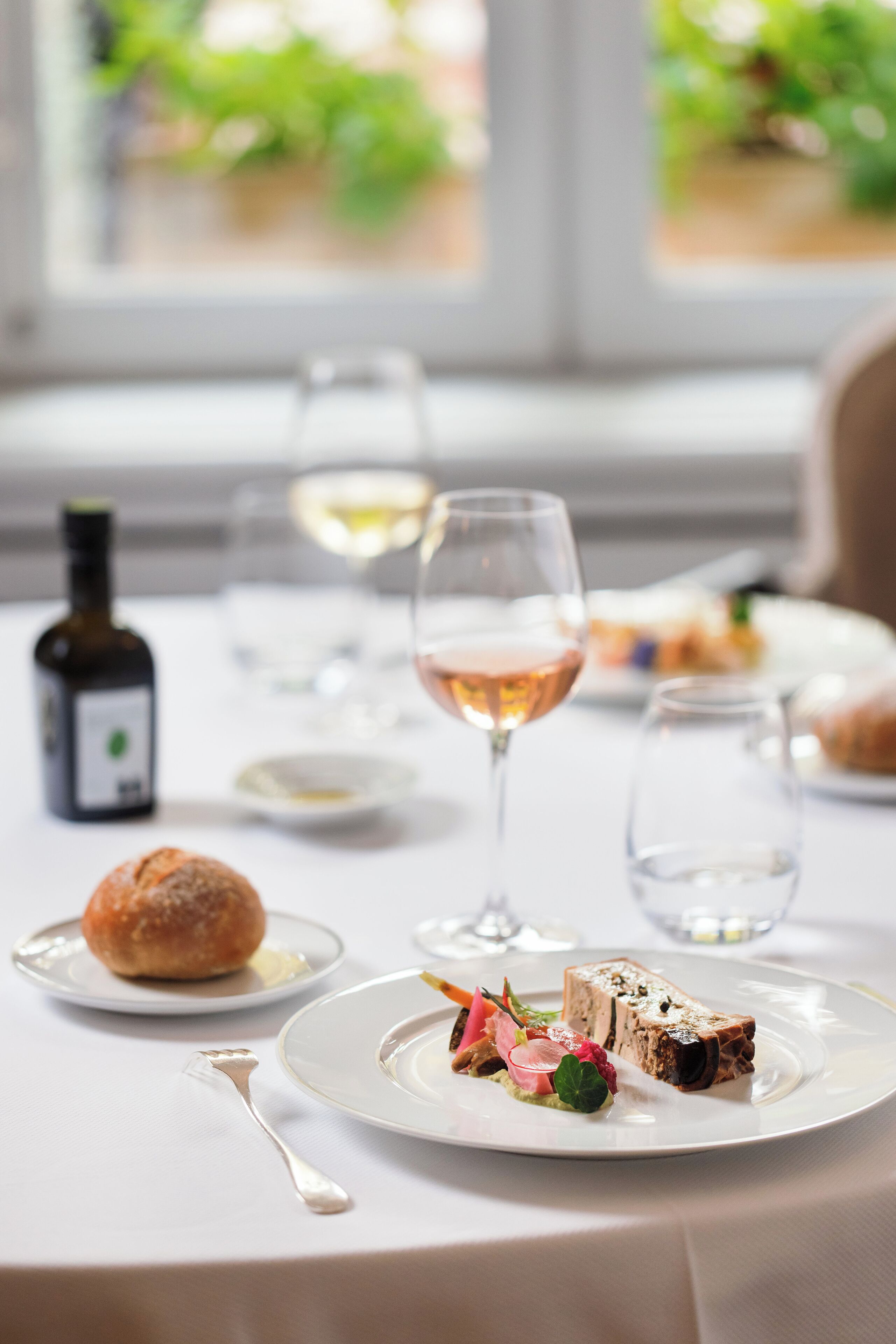 Una mesa de comedor con platos de comida, copas de vino y una botella de vino.