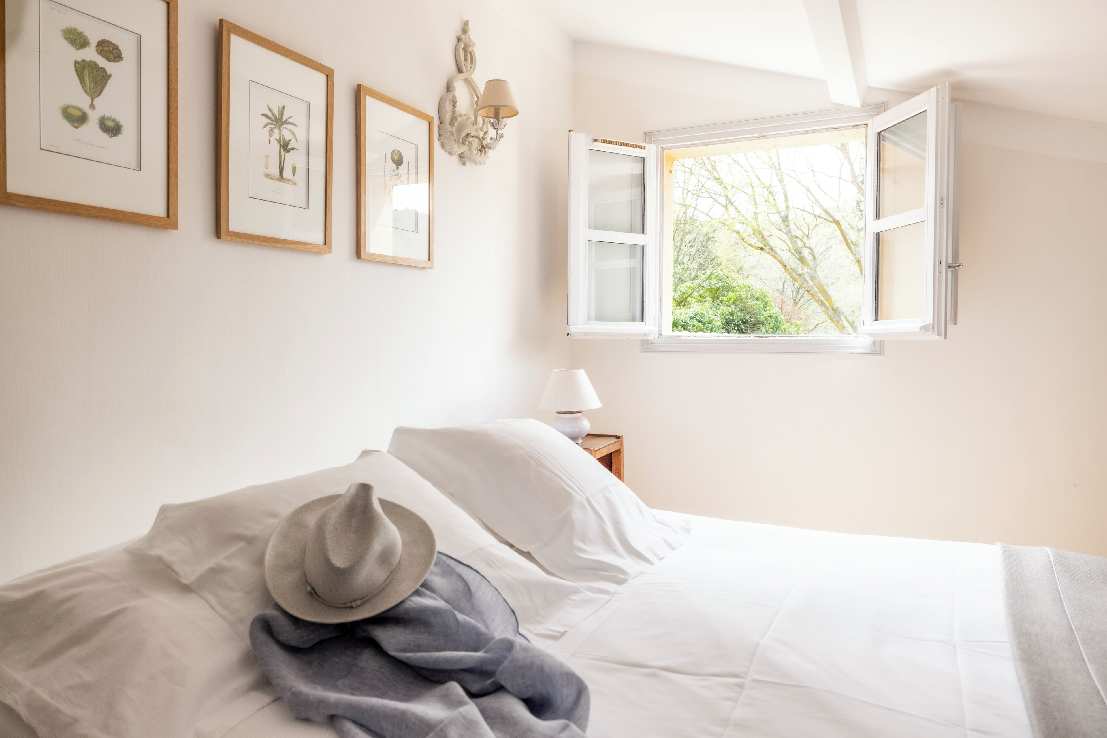 A bedroom with a bed, a hat, and framed botanical prints on the wall.