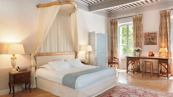 A bedroom with a four-poster bed, a desk with two chairs, and a view of the outdoors through a window.