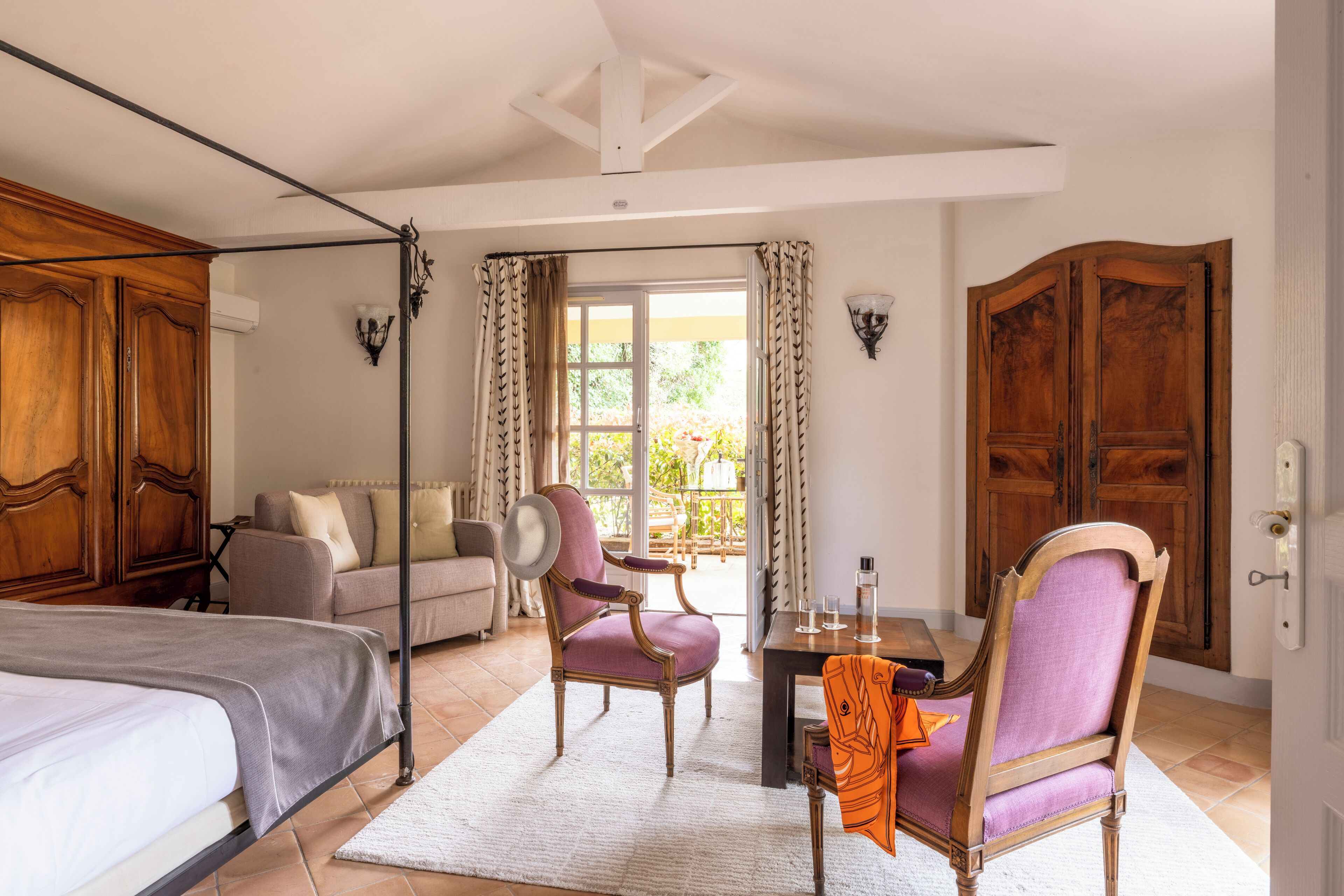 A bedroom with a bed, a chair, a sofa, and a table with a lamp.
