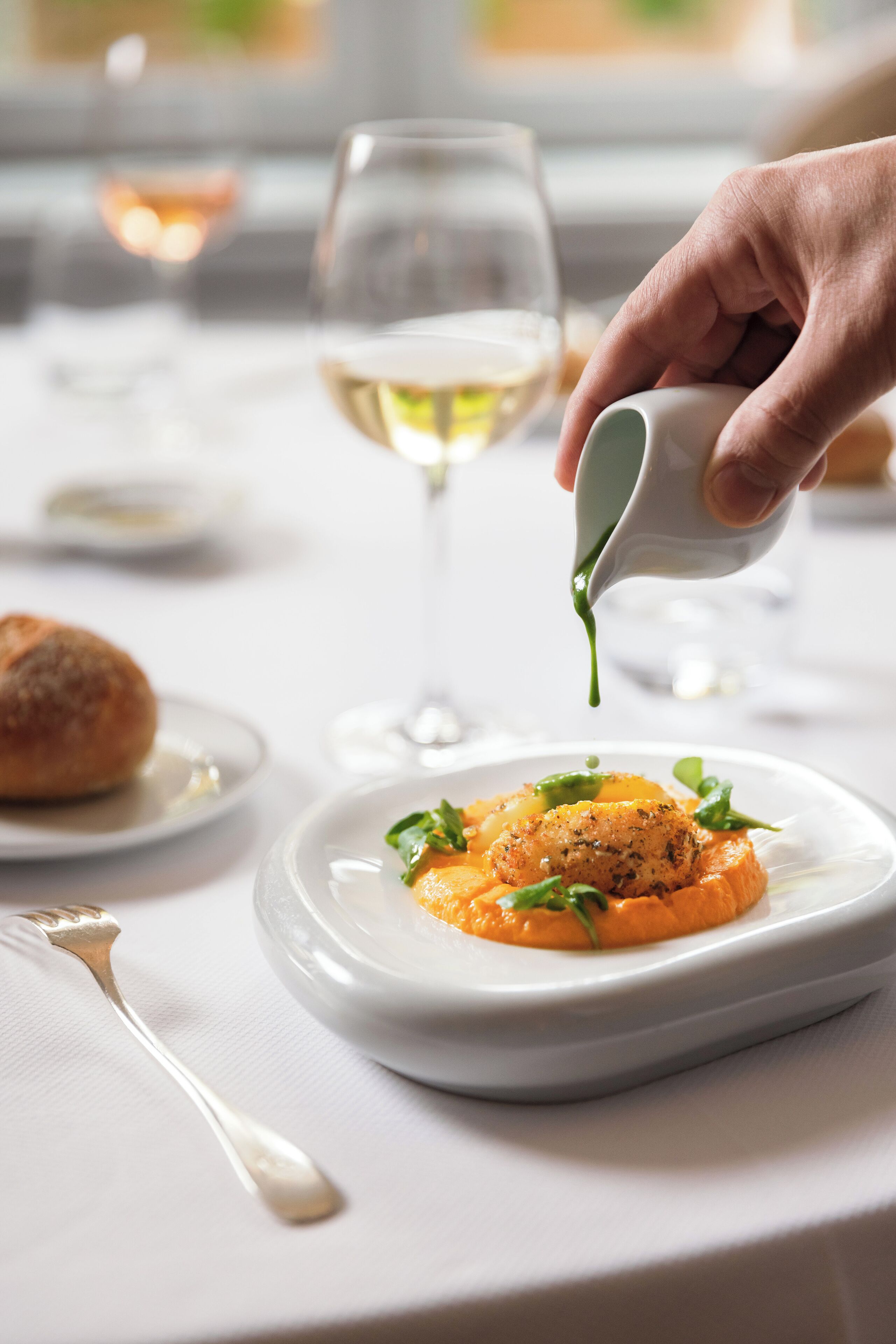 Una mesa de comedor con un plato de comida, una copa de vino blanco y una cuchara.