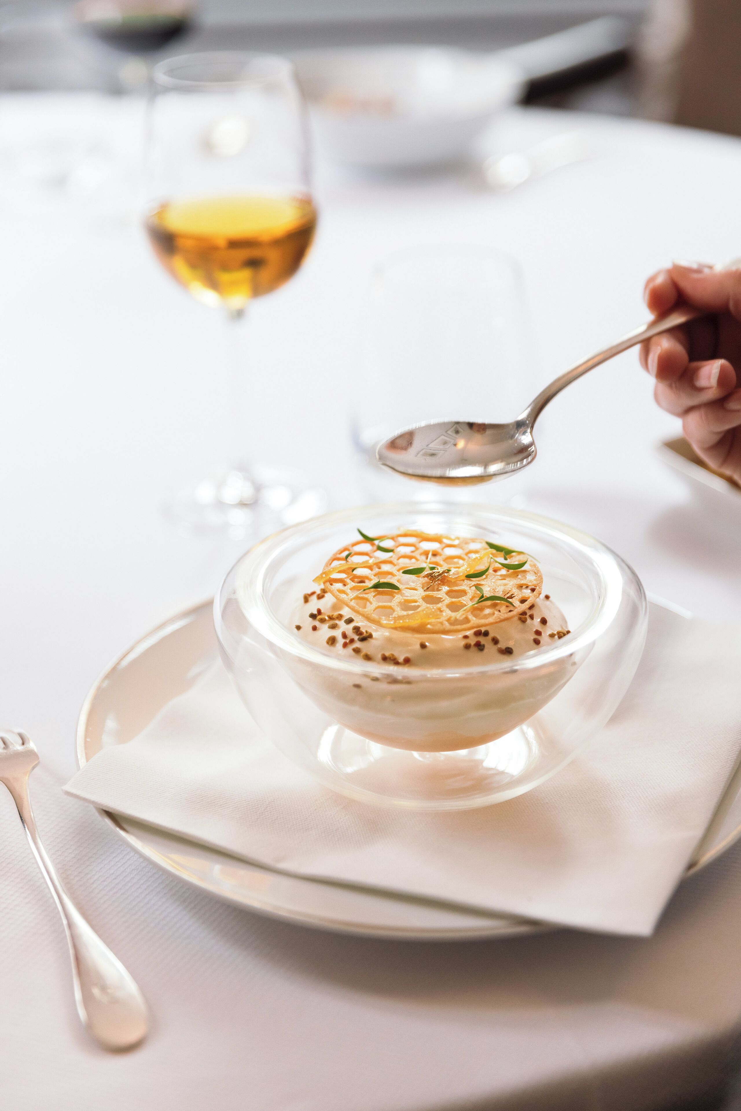 Un tazón de vidrio transparente con sopa sobre un plato blanco y una cuchara.
