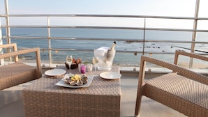 Un balcón con mobiliario de mimbre, una mesa dispuesta con ostras, copas de vino y una vela.