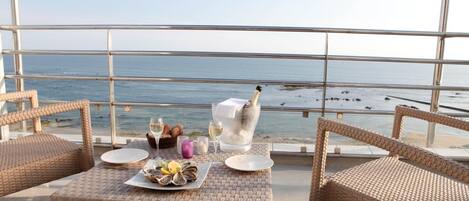 A balcony with wicker furniture, a table set with oysters, wine glasses, and a candle.