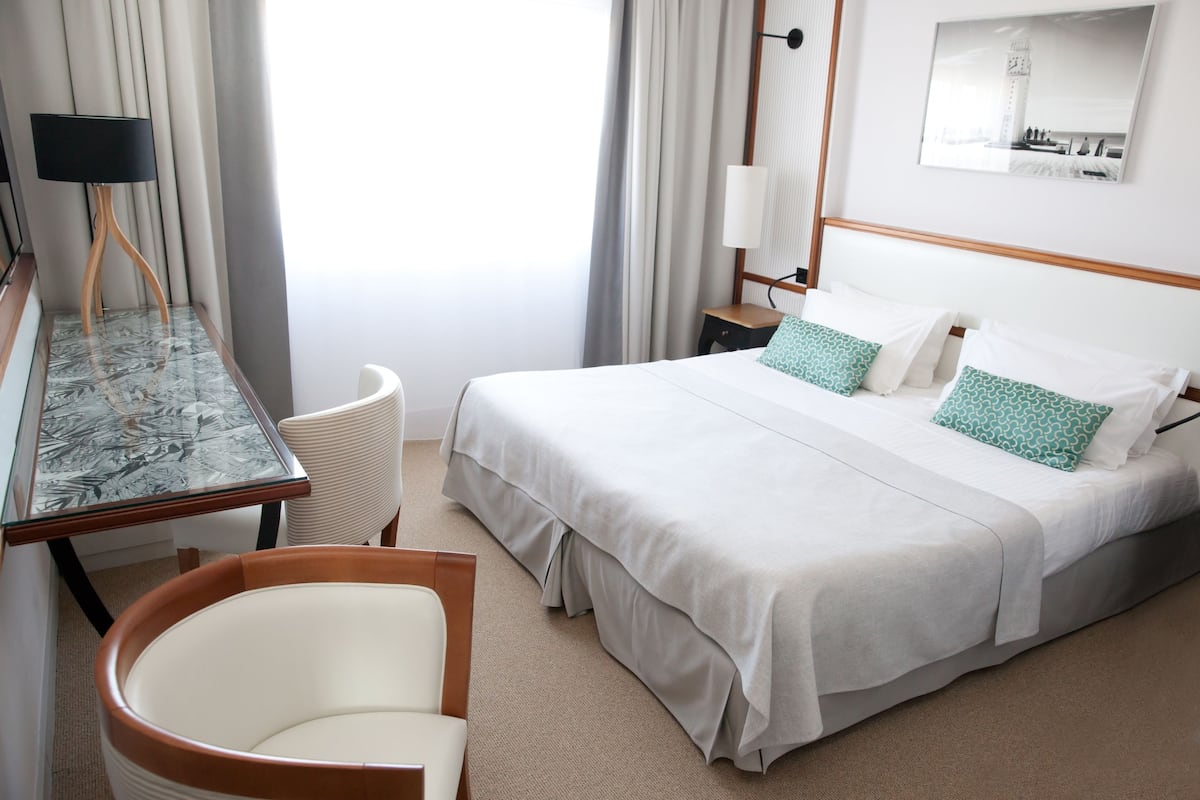A hotel room with a bed, a desk, a chair, and a lamp.