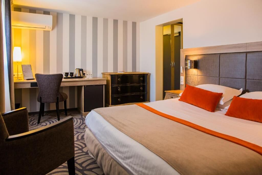 A hotel room with a bed, a desk, a chair, and a dresser.