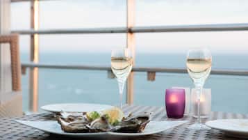 A table with two glasses of white wine, a plate of oysters, and a purple candle.
