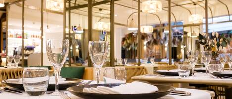 Un restaurante con mesas dispuestas para comer, que presenta un interior moderno con divisiones de vidrio e iluminación colgante.