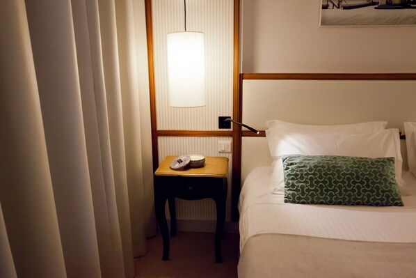 A hotel room with a bed, a bedside table with a lamp, a pillow, and a wall-mounted light fixture.