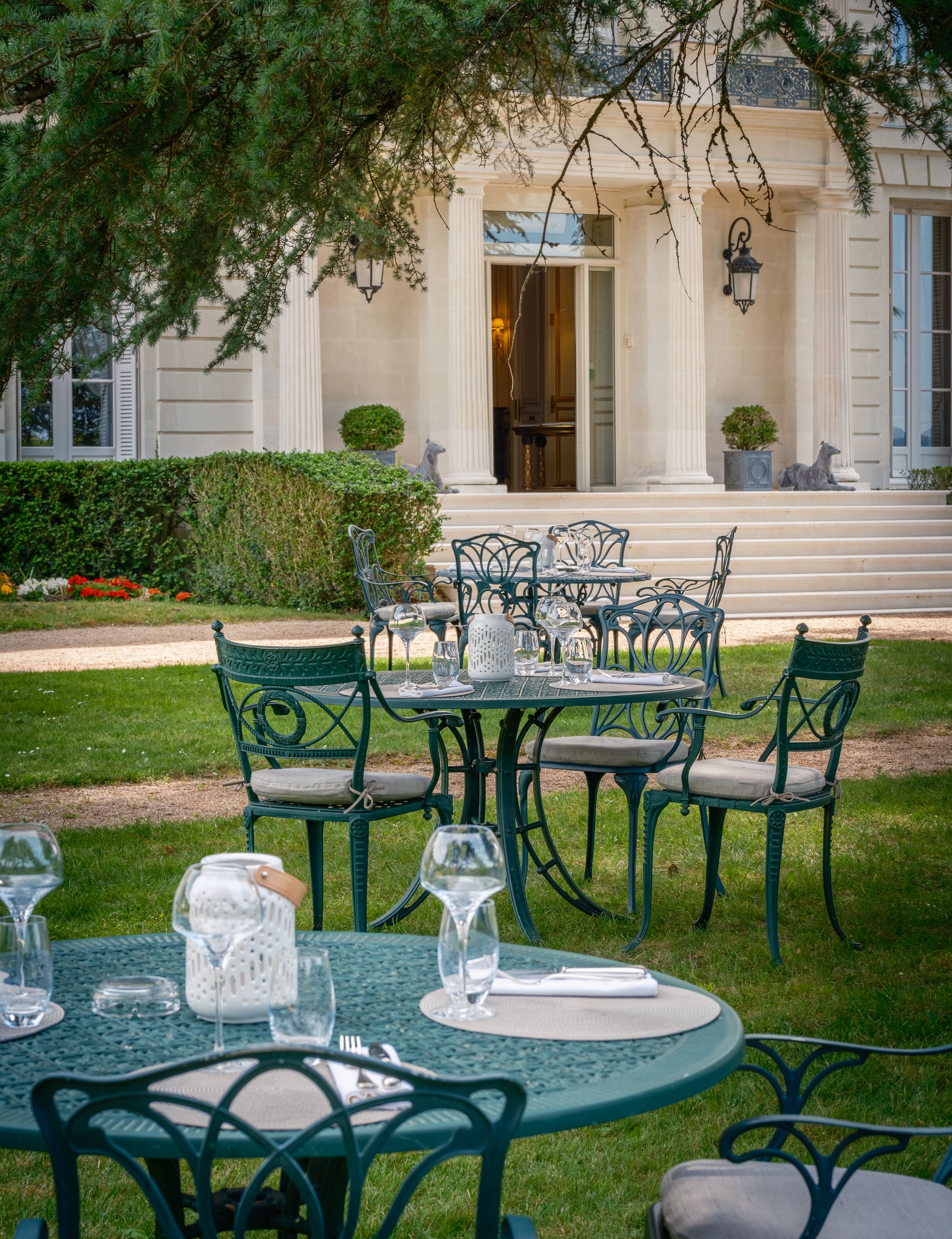 An outdoor dining area with a table set for six, surrounded by green metal chairs.