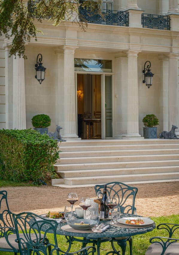 Une entrée imposante, avec des marches menant à une porte, flanquée de colonnes et agrémentée de plantes en pot.