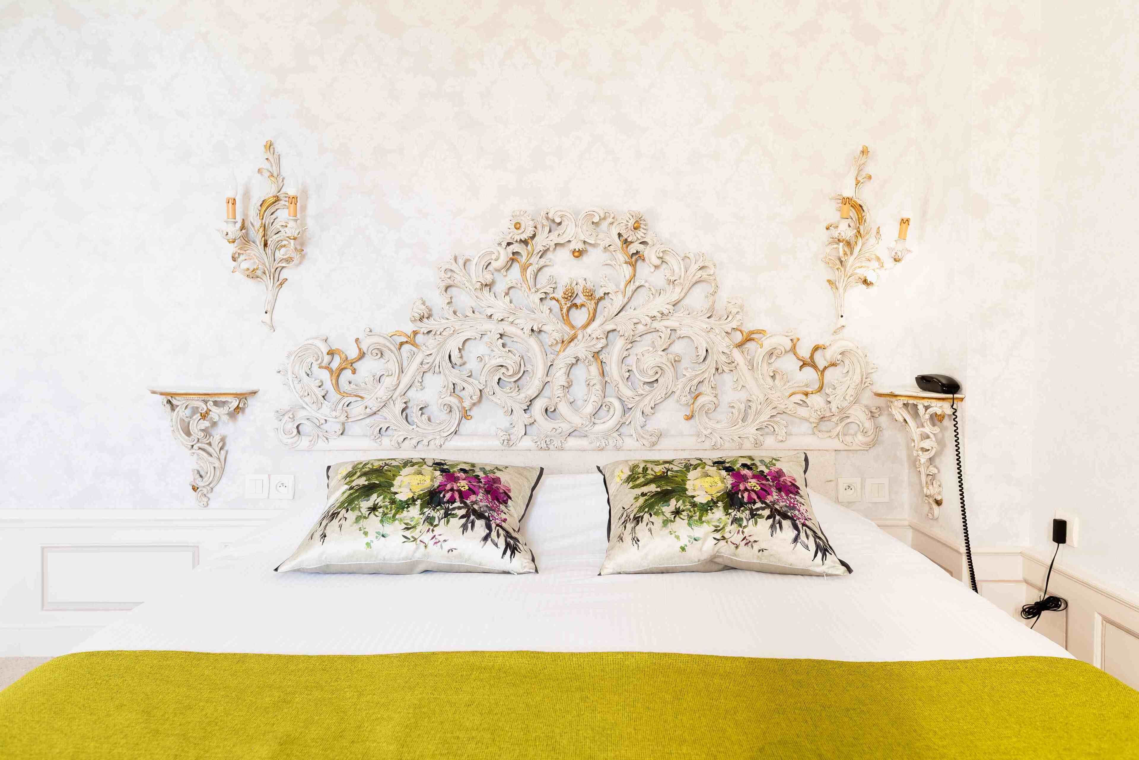 Un lit doté d’une tête de lit décorée, de coussins à motifs floraux et d’un plaid vert.