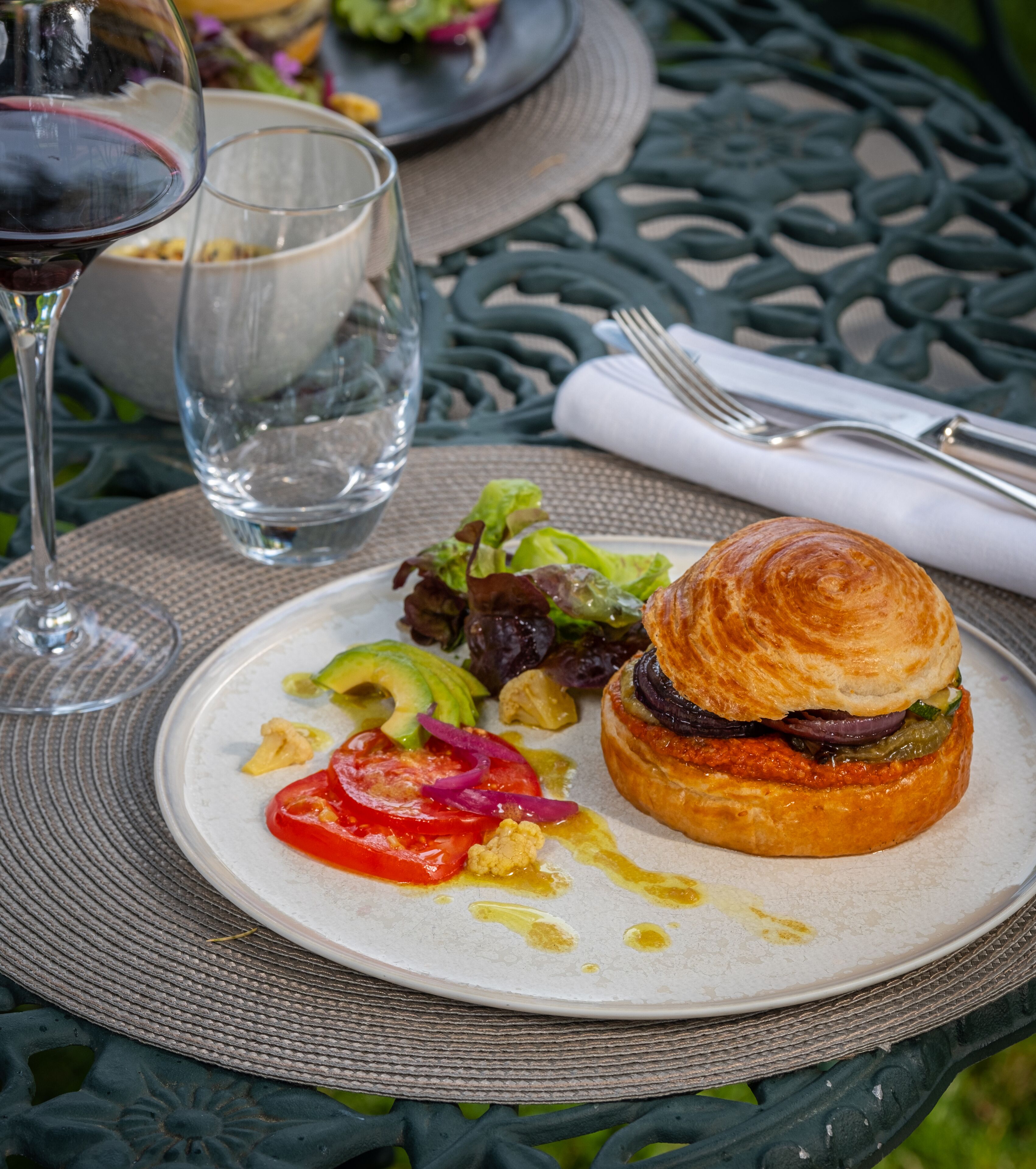 Un plato con un sándwich, ensalada y una copa de vino tinto sobre una mesa.