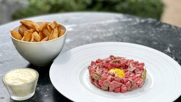 A plate of steak tartare with a raw egg yolk in the center, served with a side of potato chips and a small bowl of sauce.