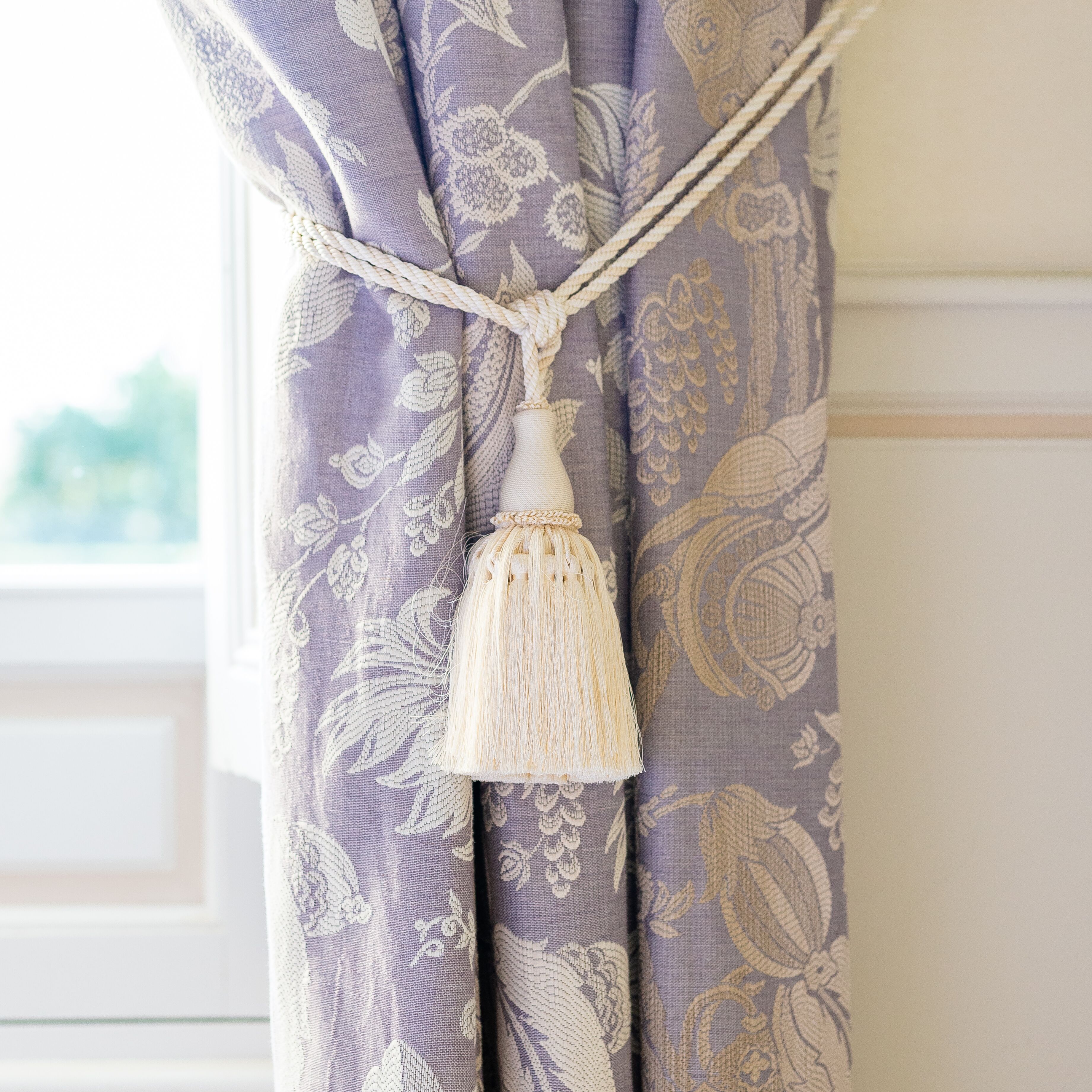 A curtain with a floral pattern and a tassel hanging from the top.