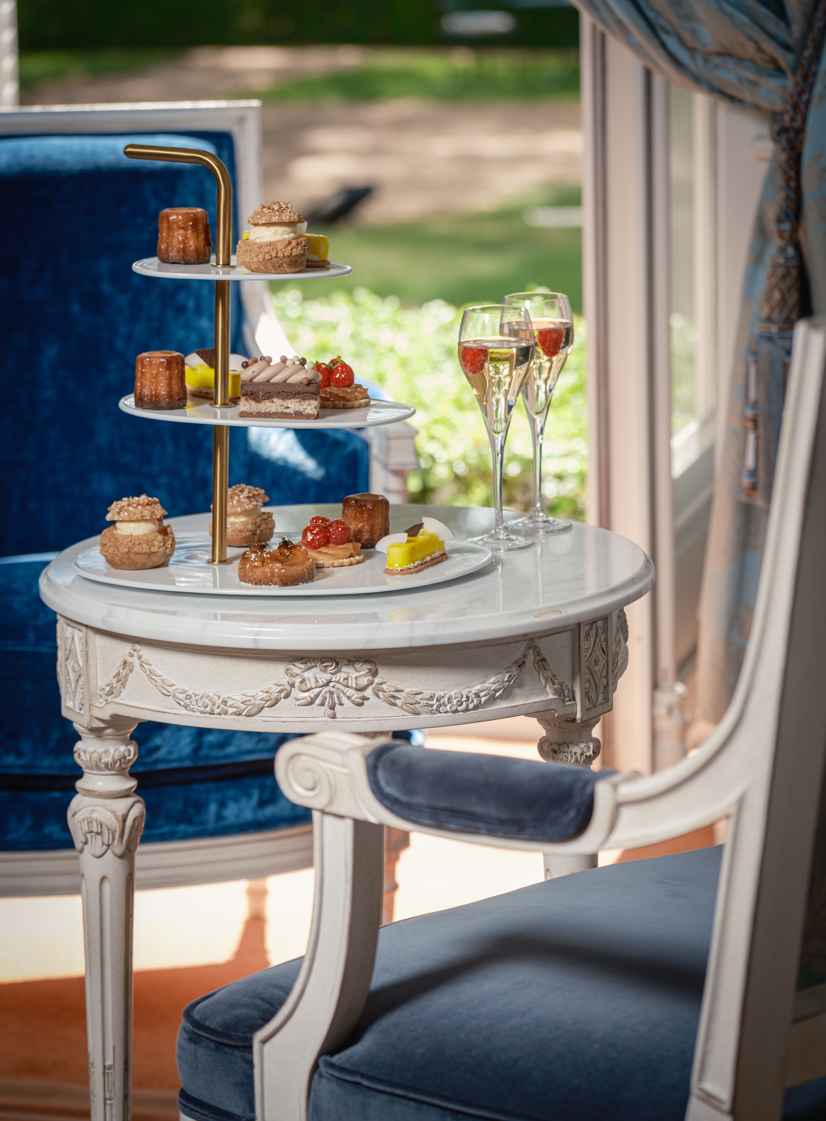 A three-tiered dessert stand with various pastries and a glass of champagne on a white table.