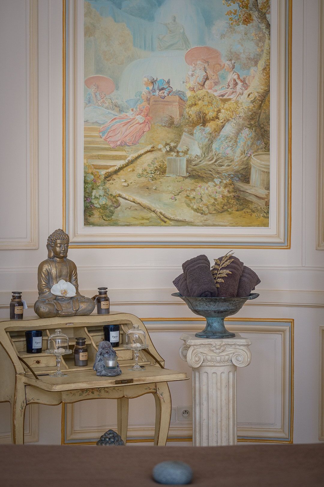 A room with a classical painting, a Buddha statue, and a table with candles and a glass.