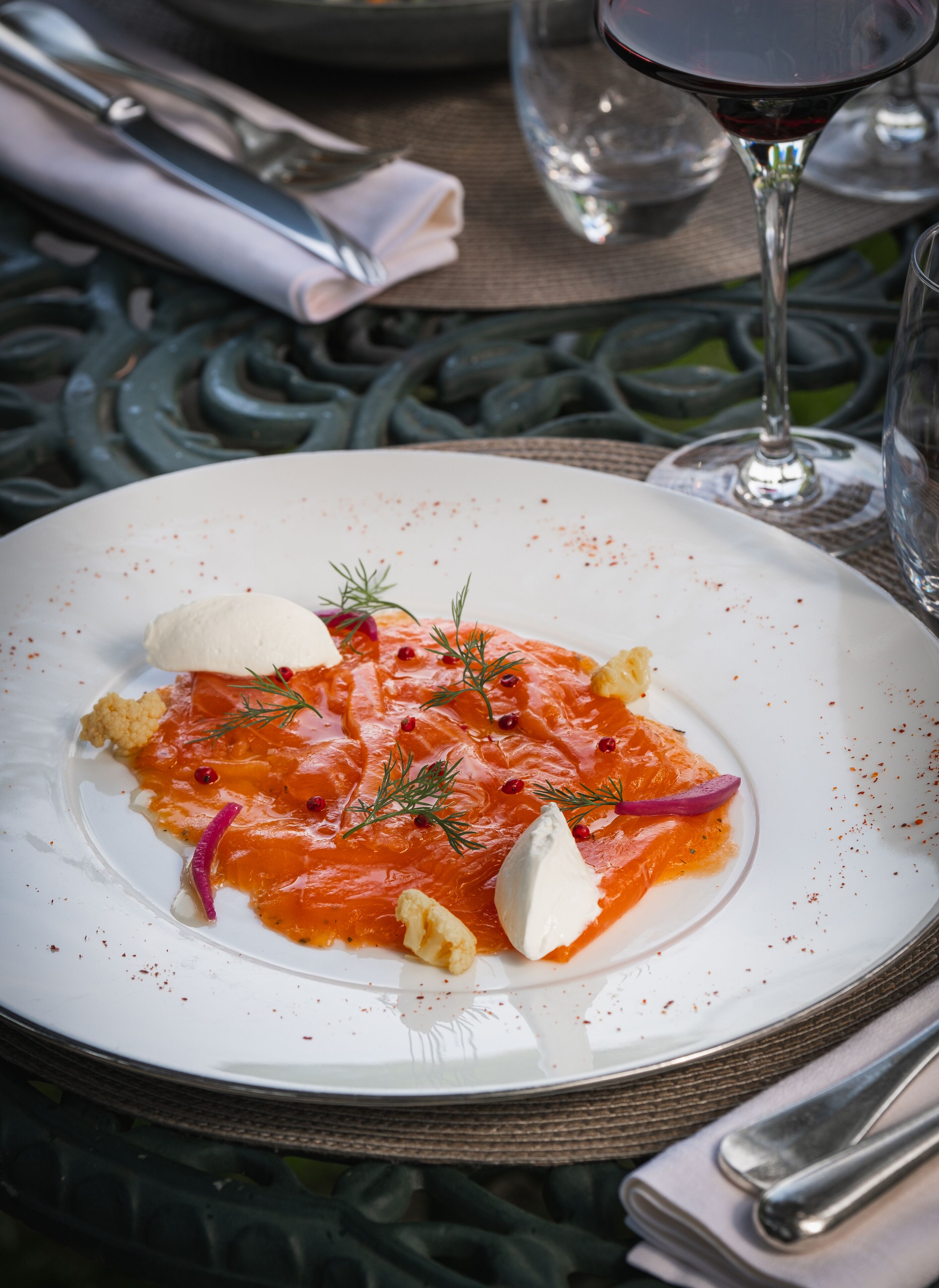 Plat blanc amb salmó, crema i guarniments sobre una taula amb un got de vi vermell.