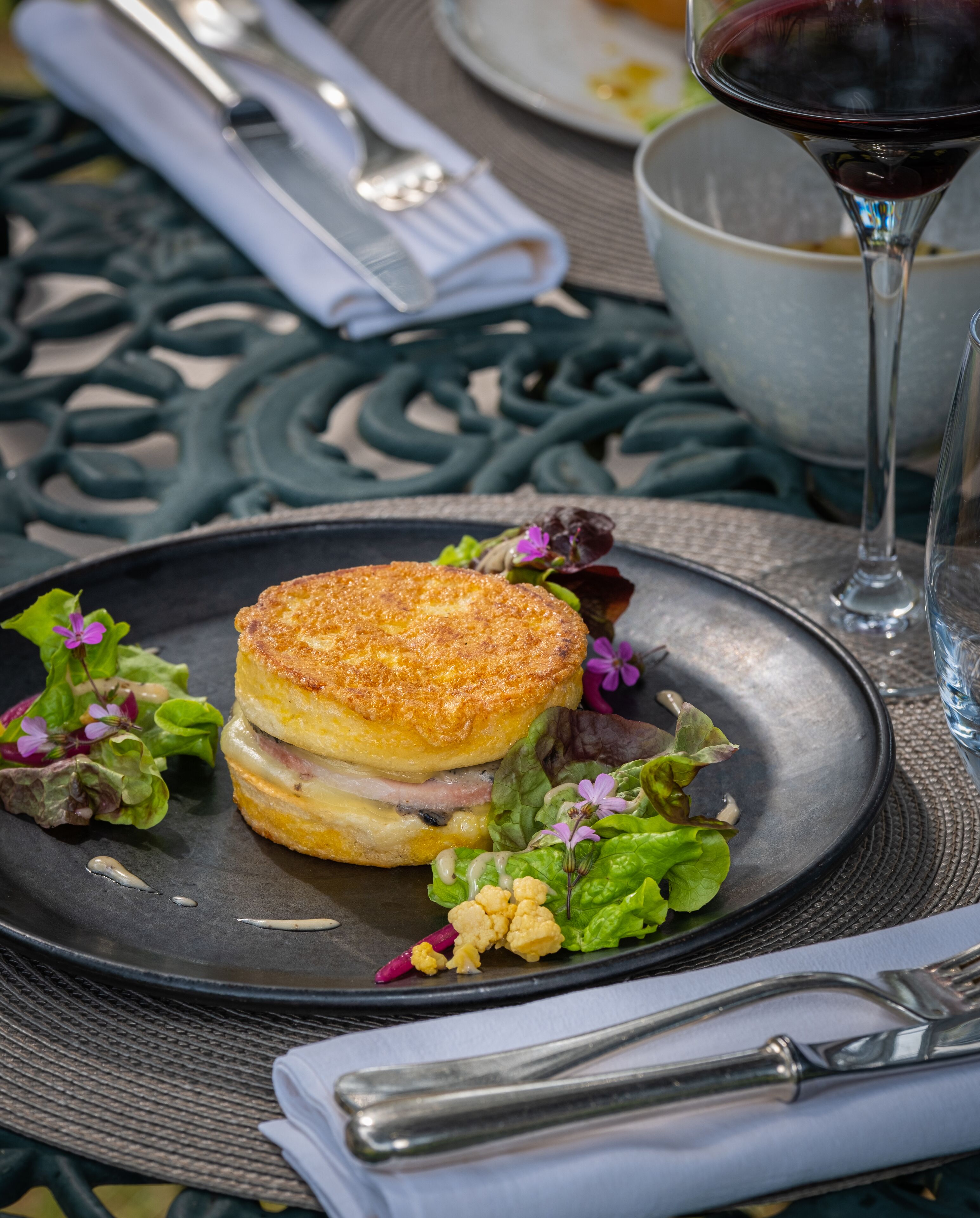 A plate with a sandwich, salad, and a glass of red wine on a table with a metal tablecloth.