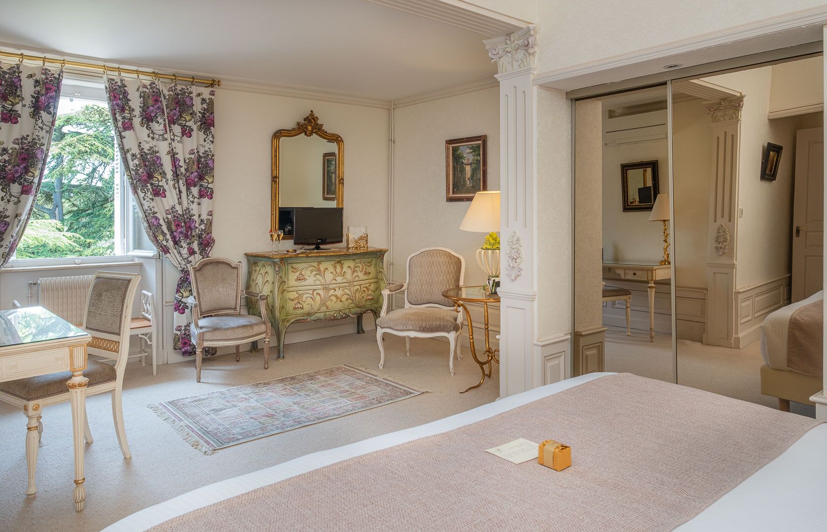 Habitación de hotel con cama, escritorio y silla, cómoda, televisor y espejo.