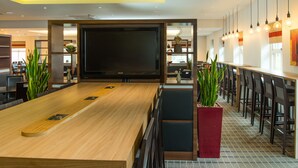 Un hall d’hôtel moderne doté d’un long comptoir d’accueil, d’un grand téléviseur à écran plat et d’un espace salon avec des chaises et des tables.