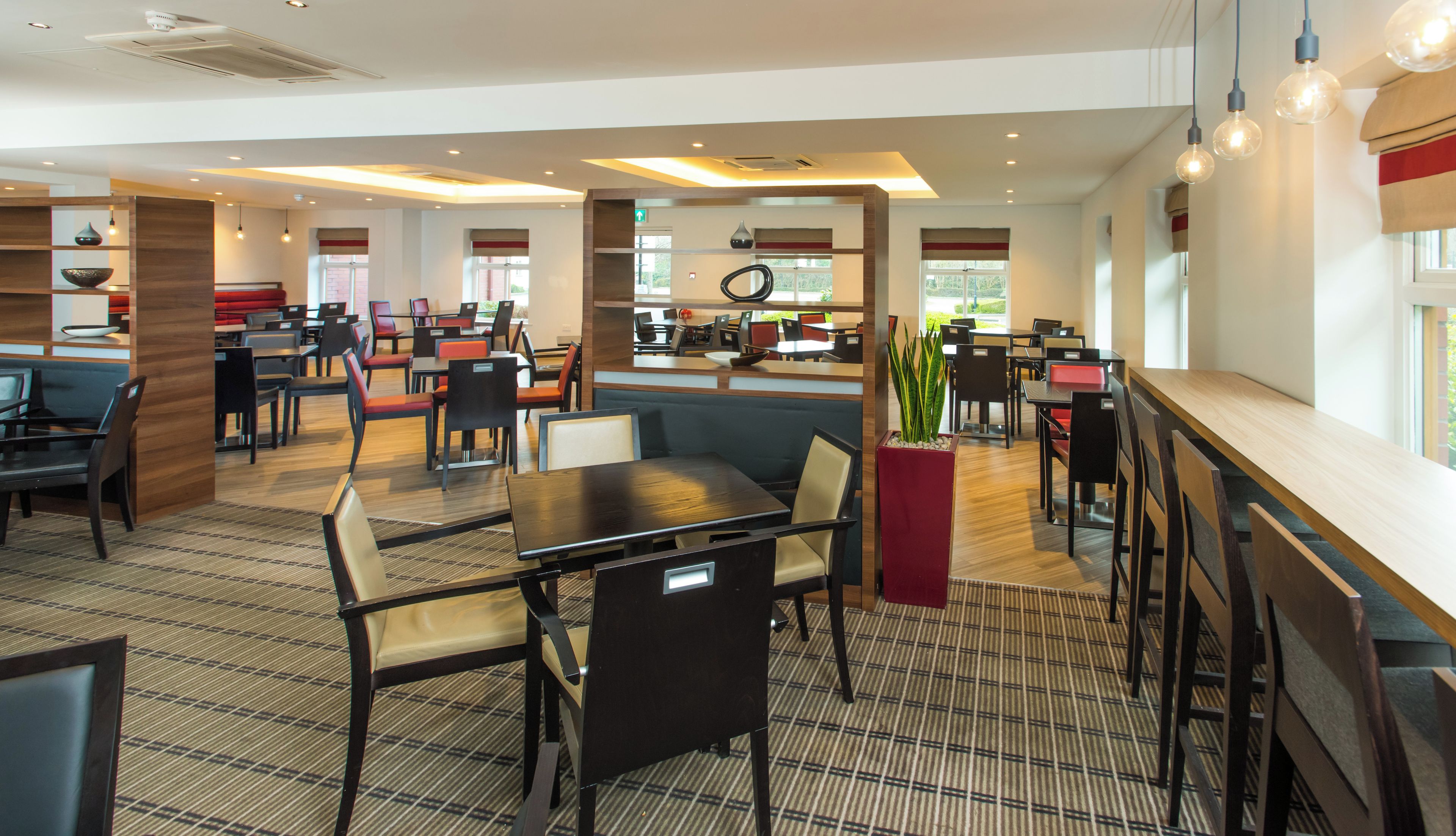 Un restaurante moderno con varias zonas de estar, incluyendo cabinas y mesas, y una barra central.