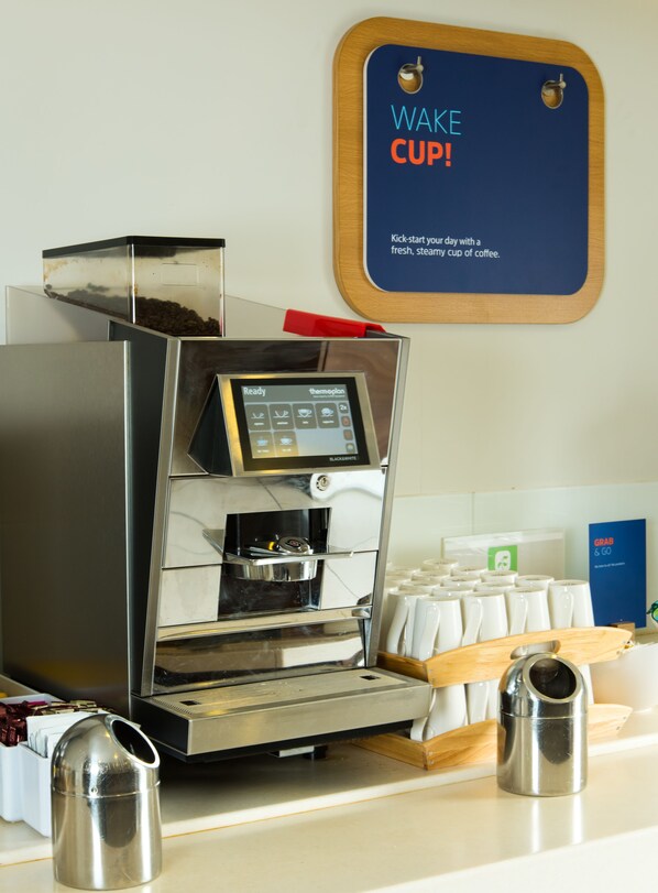 Una cafetera con pantalla digital, un molinillo de café y una taza sobre una encimera.