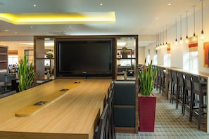 A modern bar area with a long wooden table, multiple seating options, and a large flat-screen TV.