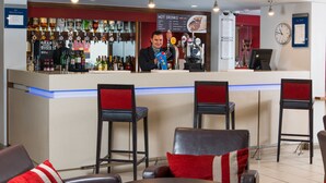 Un espace bar comprenant un comptoir, des tabourets et un coin salon avec des tables et des chaises.