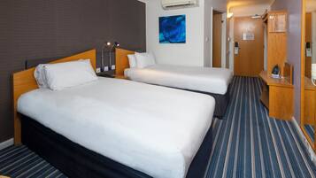 Quarto de hotel com duas camas, um quadro na parede e uma porta com interruptor de luz.