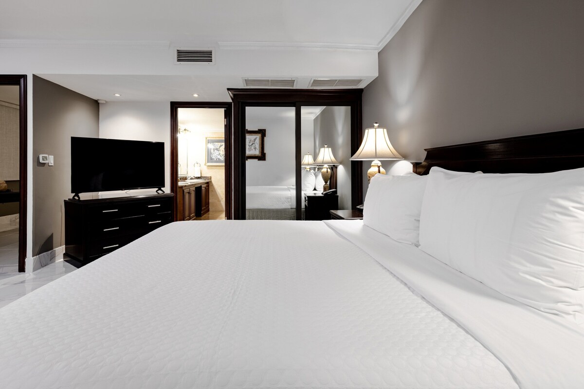 Habitación de hotel con una cama grande, televisión de pantalla plana, cómoda y mesita de noche con lámparas.