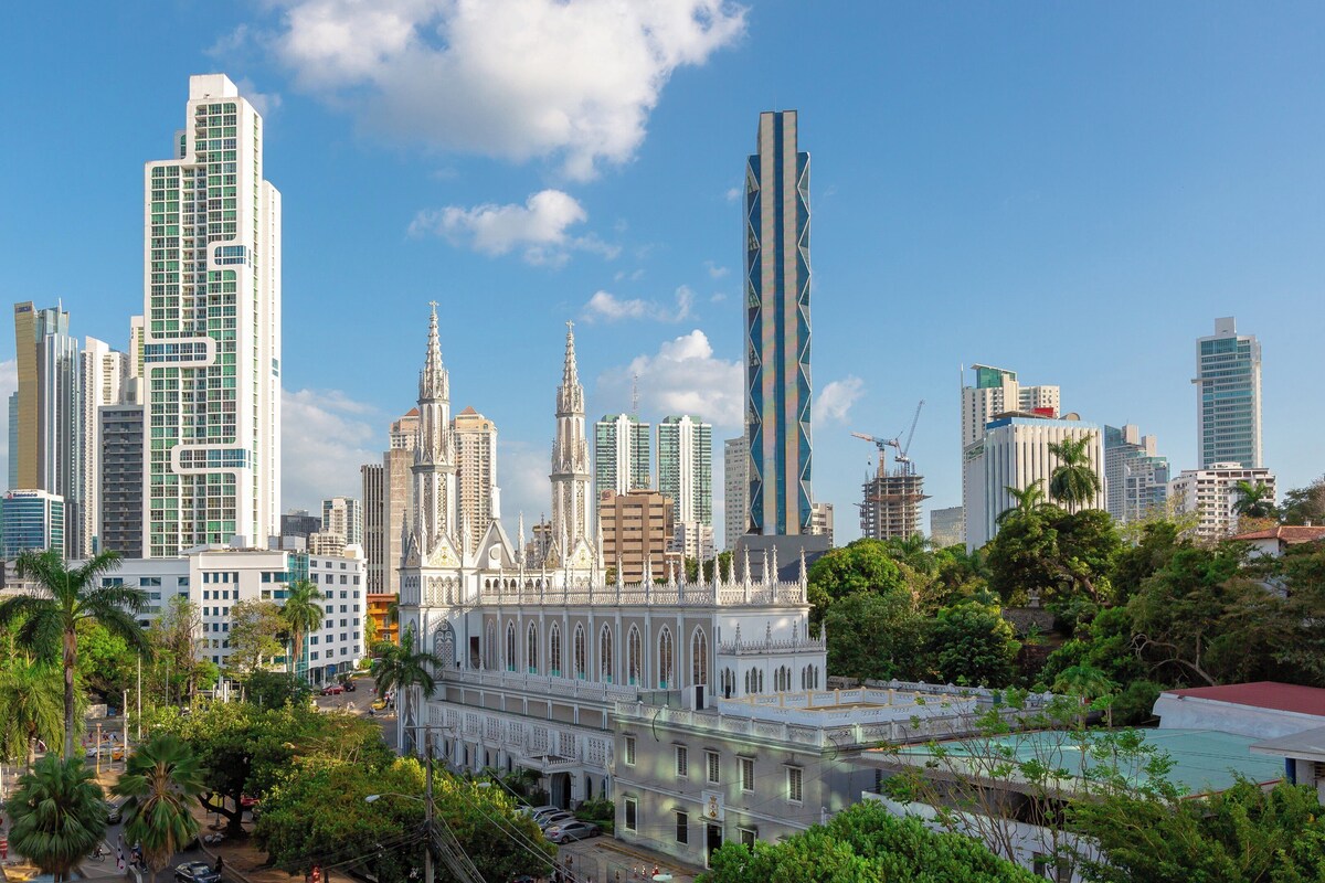 Un paisaje urbano con rascacielos modernos, un edificio histórico con arquitectura ornamentada y abundante vegetación.