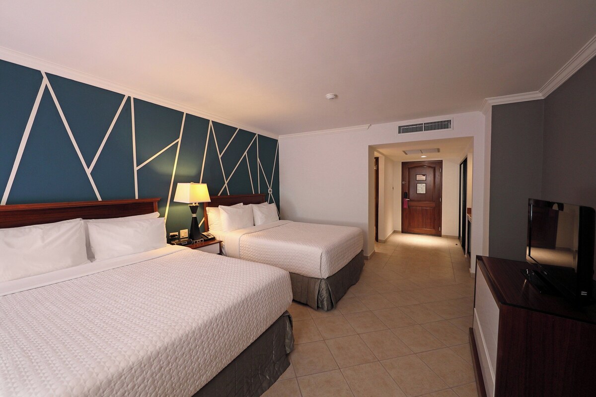 Una habitación de hotel con dos camas, televisión, escritorio y lámpara.