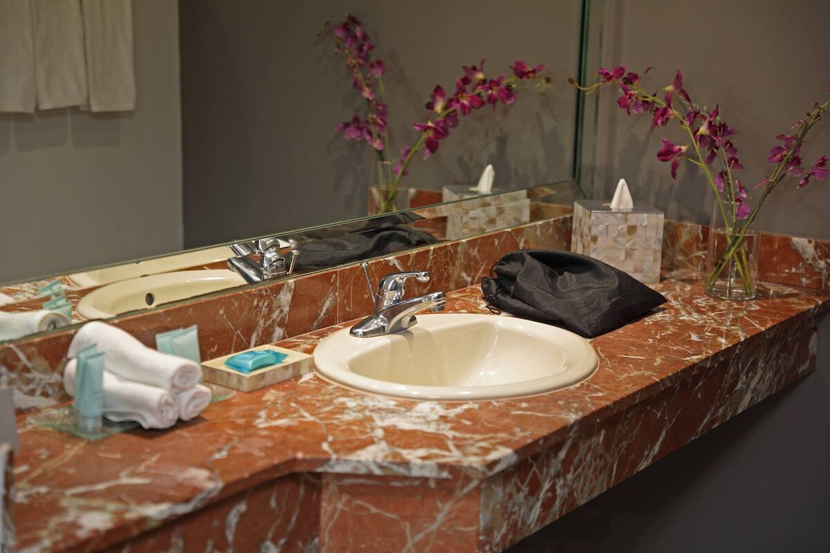 Un baño con lavamanos de mármol, un espejo y un florero con flores.