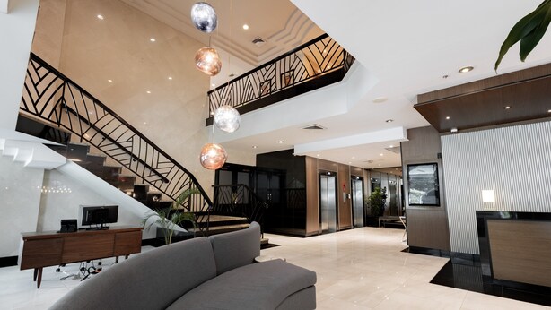 Een ruime lobby met een gebogen grijze bank, een trap met een geometrische leuning, en een receptiebalie.
