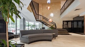 Een moderne lobby met een gebogen grijze bank, een trap met metalen leuning en hangende, bolvormige lampen.
